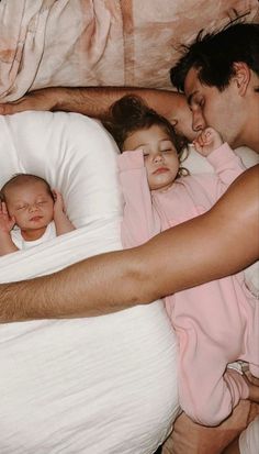 a man is sleeping with two babies in his arms and the baby has her eyes closed