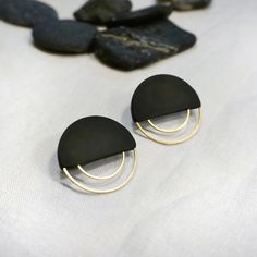 two black and gold earrings sitting on top of a white cloth next to some rocks