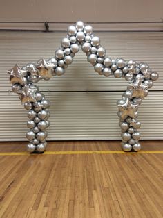 an arch made out of silver balls and stars on a wooden floor in front of a garage door