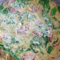 an omelet with ham, spinach and cheese in a pan on the stove