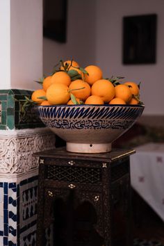 a bowl filled with oranges sitting on top of a table next to a vase