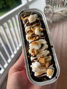 a person holding up a container filled with ice cream and toppings on top of it