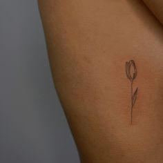 a woman's back with a single flower tattoo on her left side ribcage