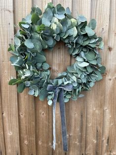 a wreath is hanging on the side of a wooden fence with a ribbon tied around it