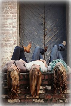 three people laying on the ledge of a brick building with their backs turned to one another