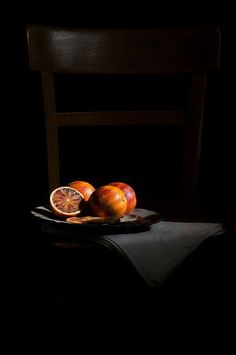 two oranges sitting on top of a wooden table next to a black chair in the dark