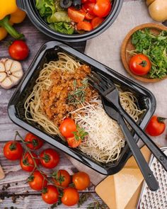 two black plastic containers filled with pasta and veggies on top of a wooden table