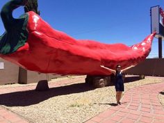 a woman standing in front of a giant red chili