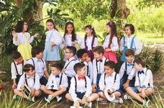 a group of young children sitting next to each other in front of trees and grass