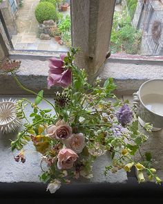 a vase filled with flowers sitting on top of a window sill next to a cup