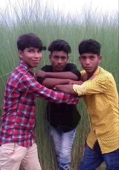 three young men are standing in front of tall grass and one is holding his arm around the other