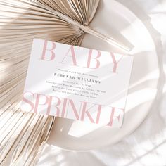 a white plate topped with a pink baby sprinkle card next to an umbrella