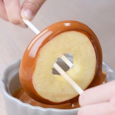 a person dipping an apple into chocolate sauce with a stick in their hand and another hand holding a spoon