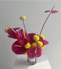 a vase filled with pink and yellow flowers on top of a white tablecloth covered surface