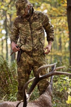 a man in camouflage is standing next to a deer with antlers on the ground