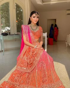 a woman in an orange and pink lehenga is posing for the camera with her hands on her hips