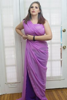 a woman in a purple dress standing by a door with her hands on her hips