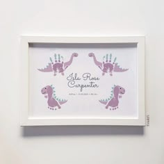 a white frame with pink and purple dinosaurs on it, in front of a white wall