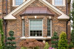 a brick house with flowers and shrubs in the front yard, along with an arched window