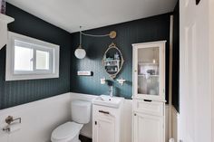 a white toilet sitting in a bathroom next to a sink under a mirror and cabinet