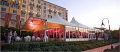 an outdoor tent with people standing around it in front of a large building at dusk