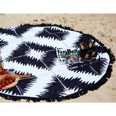 a black and white tablecloth with fruit on it sitting in the sand at the beach