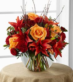 a vase filled with red and orange flowers on top of a table next to a window