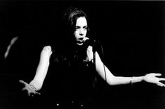 black and white photograph of a woman singing into a microphone with her hands out to the side