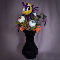 a crocheted vase with flowers in it on a purple background and an orange ribbon