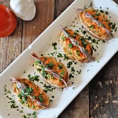 small appetizers are arranged on a white platter next to tomatoes and garlic