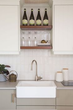 a kitchen sink with three bottles of wine on the shelf above it in front of white cabinets