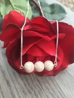 three white beads hanging from a silver chain next to a red rose on a table