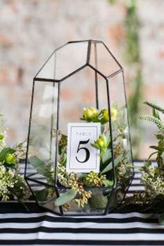 the table numbers are displayed in glass vases with greenery and flowers on them