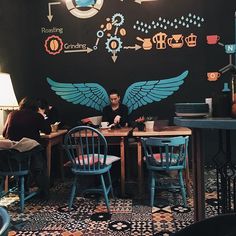 two people sitting at a table with laptops in front of them, surrounded by mechanical symbols on the wall