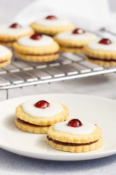 some cookies with cream and cherries on them are sitting on a plate next to a cooling rack