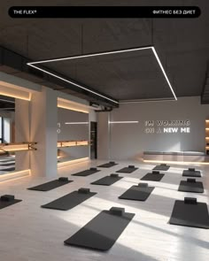 an empty gym with rows of yoga mats on the floor in front of windows and lights above them