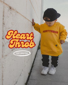 a little boy standing next to a wall wearing a yellow hoodie and black cap