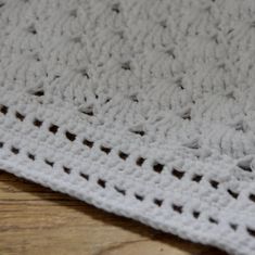 a close up of a white crocheted blanket on a wooden floor