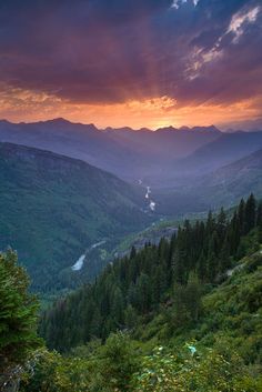 the sun is setting in the mountains with trees and grass on the hillside below it