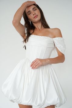 a woman in a white dress posing with her hands on her head and looking at the camera