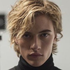 a young man with blonde hair wearing a black turtle neck sweater and looking at the camera