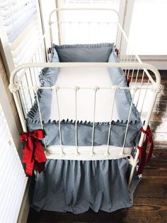 a white crib with blue and red ruffles on the bottom bed, next to a window