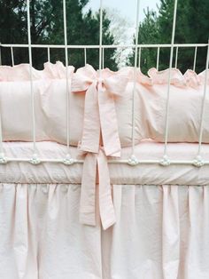 a crib with pink bedding and a bow on the top rail, in front of some trees