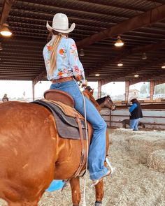 a woman riding on the back of a brown horse in a barn filled with hay