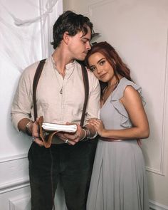 a man and woman standing next to each other in front of a white wall wearing suspenders