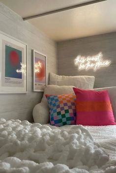 there is a bed with white sheets and colorful pillows on it, along with two framed pictures