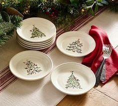 four white plates with christmas trees on them are sitting next to a red napkin and silverware