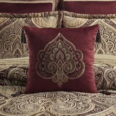 a bed with red and gold comforters and pillows on top of it, in front of a white wall