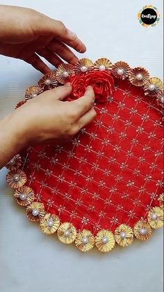 someone is making a red and gold doily with flowers on the edge that they are holding in their hands