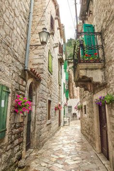 an alley way with stone buildings and green shutters on each side, flowers in the window boxes